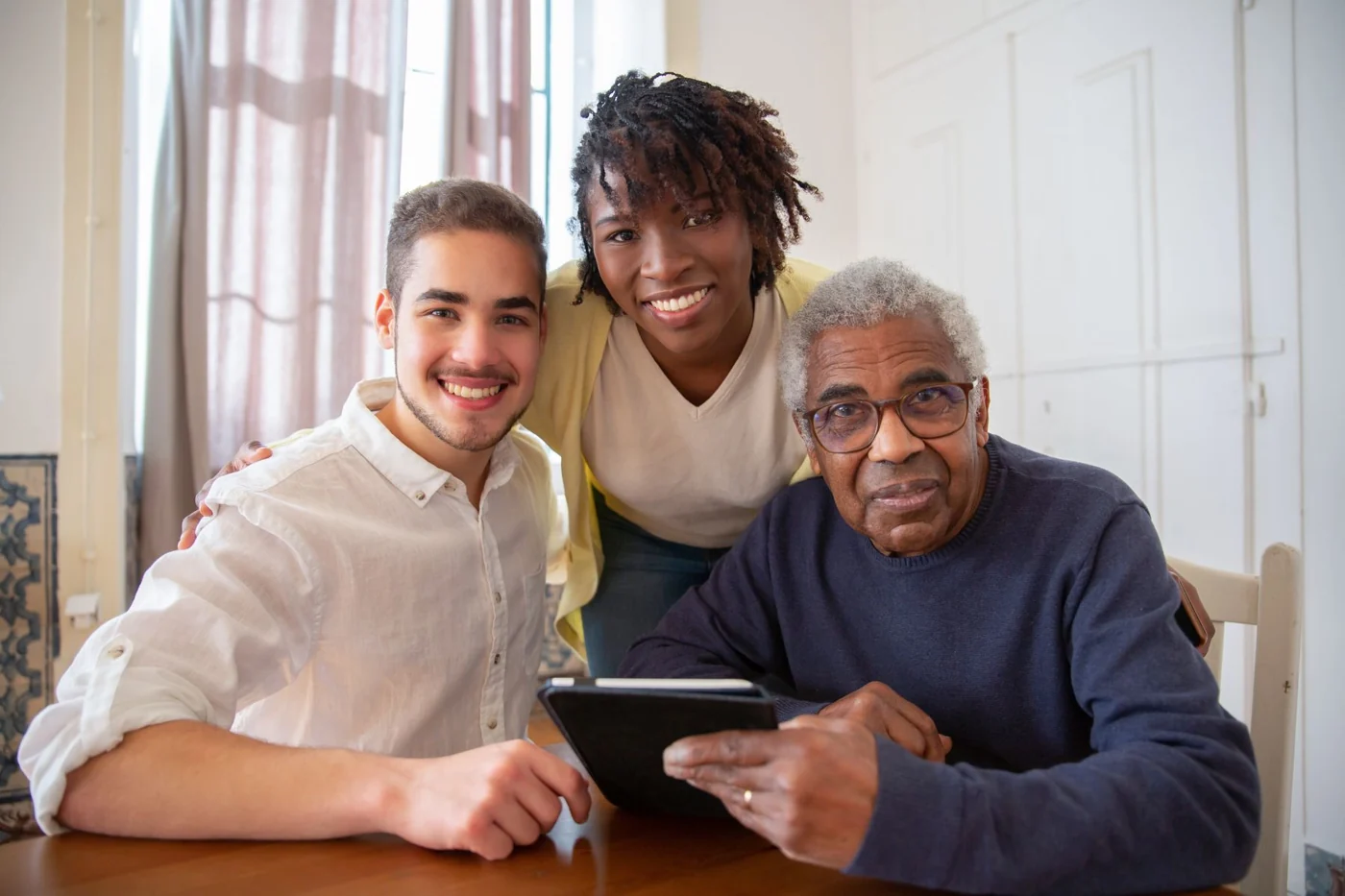 An older man and two younger adults smiling together at home