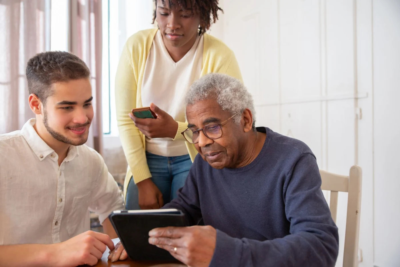 An older man and two younger adults looking at a tablet together
